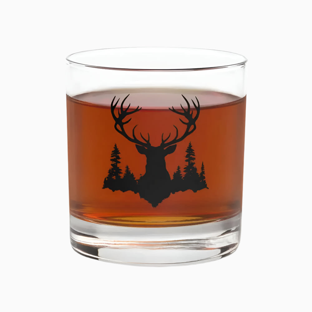 The 10.5 oz Deer Hunter Whiskey Glass, Bourbon Glass features a black stag and trees silhouette, offering a timeless design that beautifully complements the rich brown liquor inside.