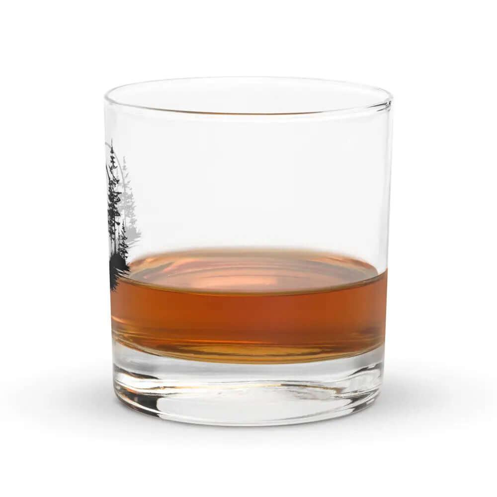 The 10.5 oz Deer Treeview Rocks Glass, designed for whiskey and bourbon, features a printed tree design and contains a small amount of amber liquid against a white background.