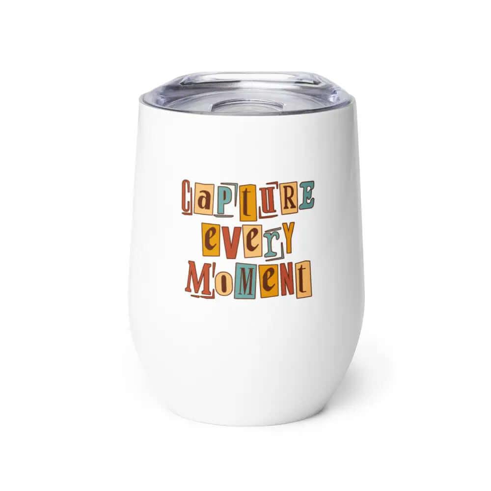 The 12 oz Capture Every Moment Wine Tumbler is a white stainless steel travel mug with a clear lid, featuring playful colorful lettering and double-wall vacuum insulation to keep drinks at the perfect temperature.