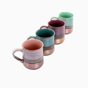 A set of four 18 oz. assorted stoneware mugs, each with a copper bottom and pastel interior, is arranged diagonally on a white background. Dishwasher safe.