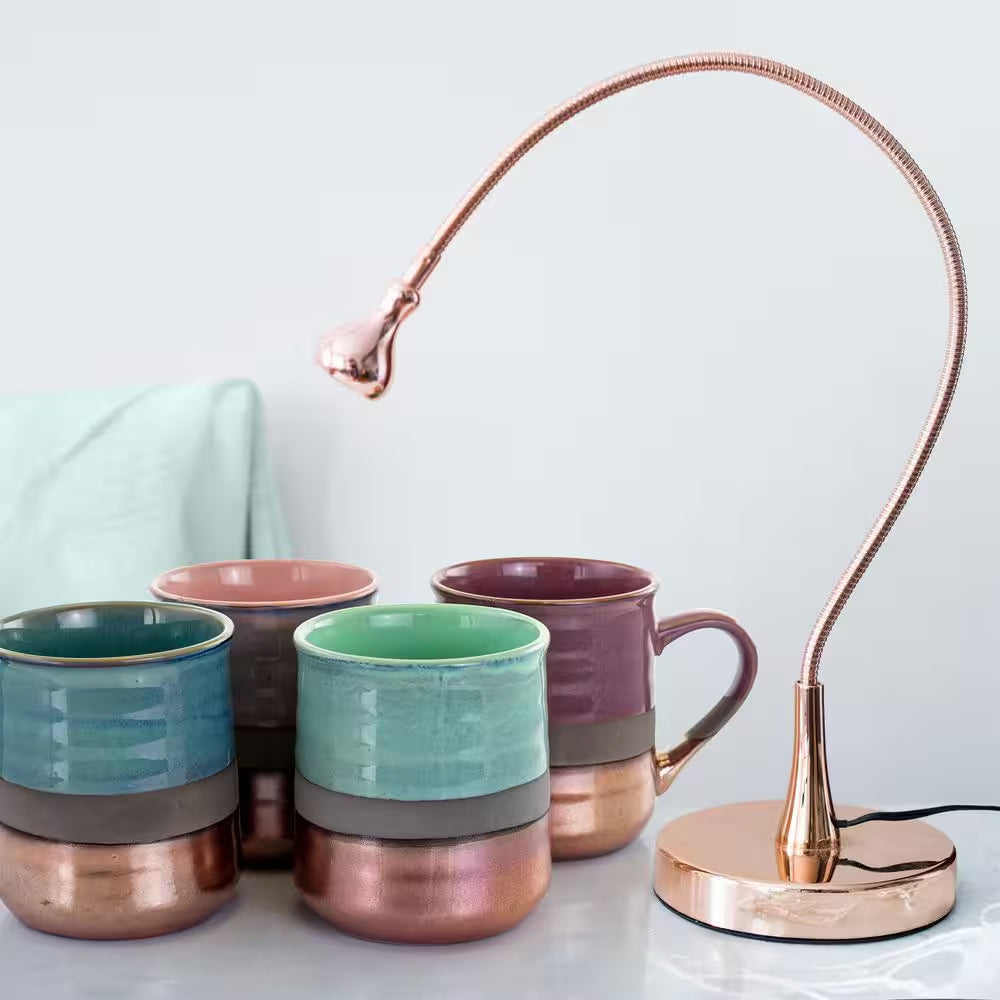 A set of four 18 oz. assorted stoneware mugs is displayed beside a rose gold adjustable desk lamp on a white surface.