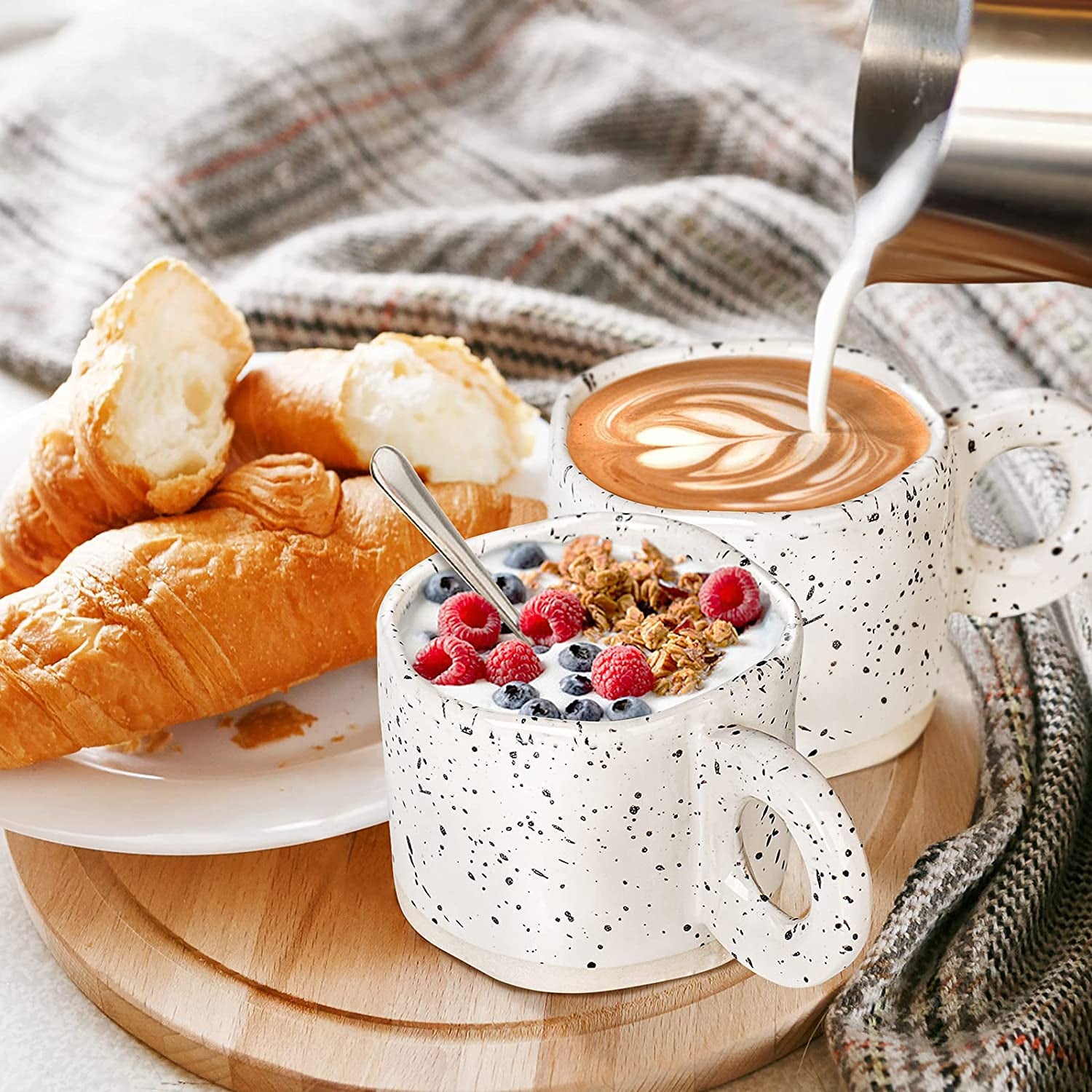 Two croissants and granola with berries are served on a wooden board beside coffee being topped with milk in ceramic coffee mugs from the 10oz Stoneware Coffee Cups Set of 4, with a checkered cloth in the background.