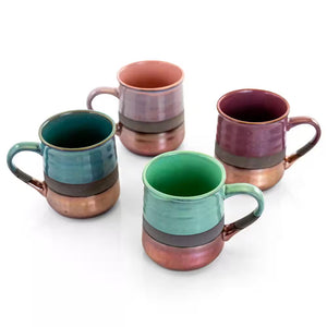 The 18 oz. Assorted Stoneware Mug Set (4-pack) features green, teal, purple, and mauve mugs with metallic copper bottoms, arranged on a white surface.