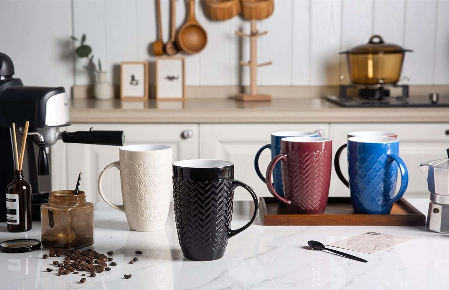 Six large 22oz ceramic coffee mugs from the Large Coffee Mugs Set are arranged on a kitchen counter with coffee accessories. Each mug is lead and cadmium free, ensuring safe use for your daily coffee needs.