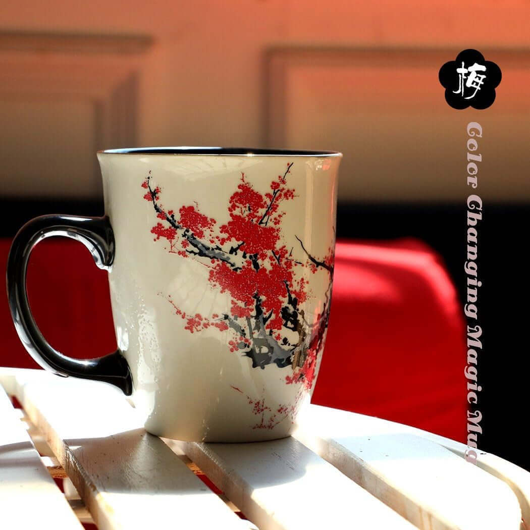 A Color Changing Heat Sensitive Magic Porcelain Mug 16oz with a black handle and a red and black floral design rests on a white slatted surface against a red background. "Color Changing Magic Mug" is written vertically on the right.