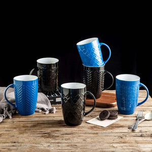 The Large Coffee Mugs Set of 6 (22oz Ceramic Tall Coffee Mugs)—three blue, three black with embossed patterns—are arranged on a wooden table with cookies, forks, and cloths. Lead and cadmium free, perfect for your favorite drinks.