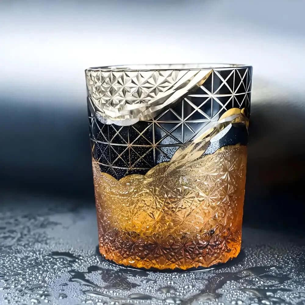 An 8 oz Crystal Whiskey Glass, crafted with Japanese craftsmanship, holds a golden-brown drink and sits on a wet surface surrounded by droplets.