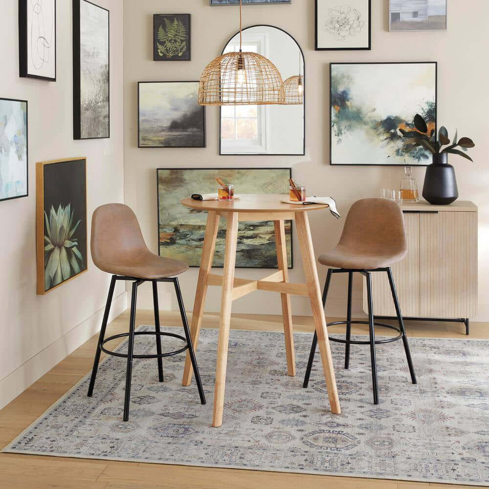 A modern room features a high round wooden table set with the Elle Fluted Double Old Fashion Whiskey Glasses (10 oz., Set of 2), two brown barstools, a patterned rug, wall art, a mirror, a sideboard, and a rattan pendant light.