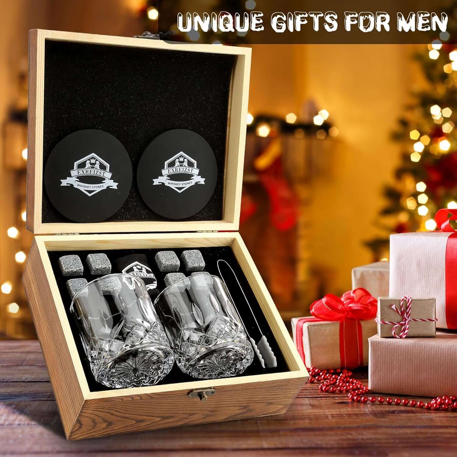 A Whiskey Stones Gift Set with two whiskey glasses, granite chilling rocks, coasters, and tongs sits open by wrapped gifts and a Christmas tree. Text reads: Unique Gifts for Men.