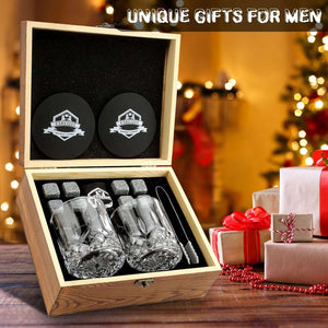 A Whiskey Stones Gift Set with two whiskey glasses, granite chilling rocks, coasters, and tongs sits open by wrapped gifts and a Christmas tree. Text reads: Unique Gifts for Men.