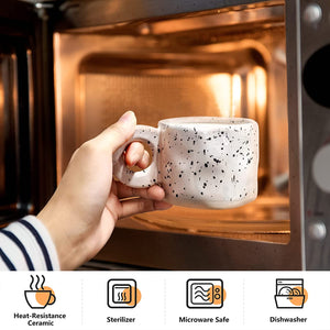 A hand places a white, speckled Ceramic Coffee Mug (10oz) from the Set of 4 into a microwave. Icons below show these stoneware cups are heat-resistant, sterilizable, and dishwasher- and microwave-safe for daily use.