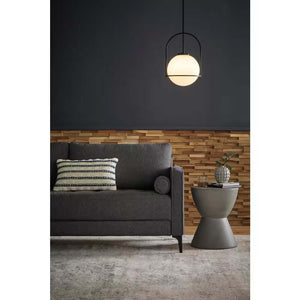 Modern living room with a dark gray sofa, striped pillow, round side table featuring the Elle Fluted Double Old Fashion Whiskey Glass - 10 oz. (Set of 2) and a small plant, plus a spherical pendant light against a wood and dark painted wall.