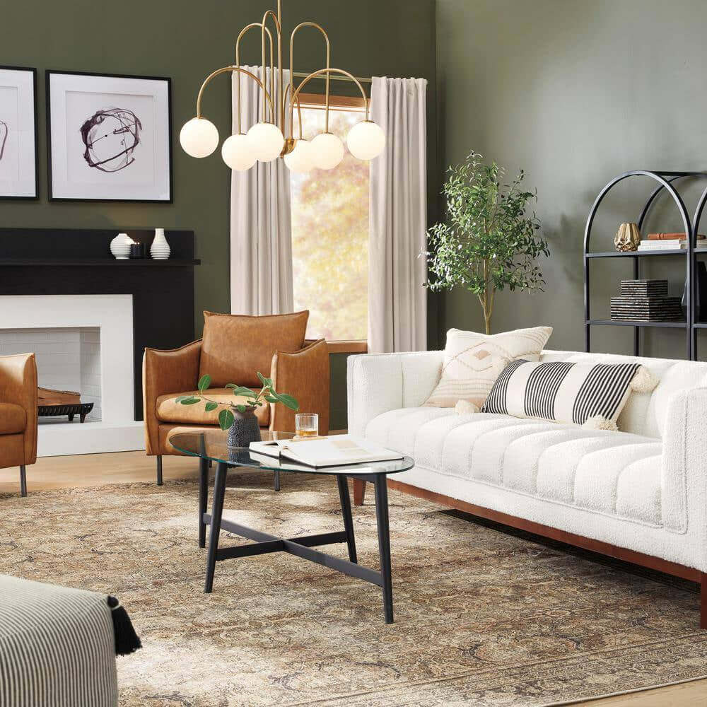 Modern living room with a white sofa, two brown leather chairs, glass coffee table topped with Elle Fluted Double Old Fashion Whiskey Glasses (10 oz., set of 2), patterned rug, abstract art, potted plant, and a gold chandelier.