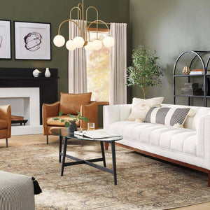 Modern living room with a white sofa, two brown leather chairs, glass coffee table topped with Elle Fluted Double Old Fashion Whiskey Glasses (10 oz., set of 2), patterned rug, abstract art, potted plant, and a gold chandelier.