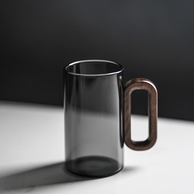 The Fiorella Smoky Fashioned Drinking Glass set (2pcs, 11oz) features transparent black glass and large oval wooden handles, showcasing minimalist elegance on a white surface against a dark background.