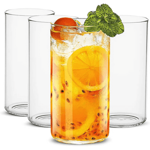 Four stylish Thin Highball Glasses (19 oz) are shown, with one in front filled with an iced citrus drink, garnished with mint, orange, and passion fruit—an elegant set ideal for serving refreshing beverages.