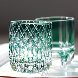 Two green-tinted Macchiaco Fashion Hand Carved Crystal Glass Cups are shown on a white surface: the front cup has a diamond-cut pattern, while the rear is plain and smooth, both illuminated by natural light.