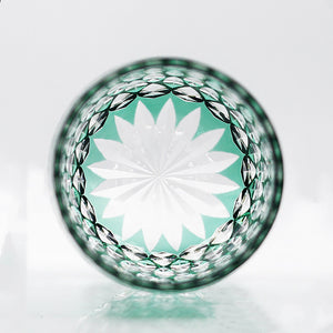 A top view of the Macchiaco Fashion Hand Carved Crystal Glass Cup shows an intricate white and green starburst pattern, framed by a textured, diamond-cut rim.