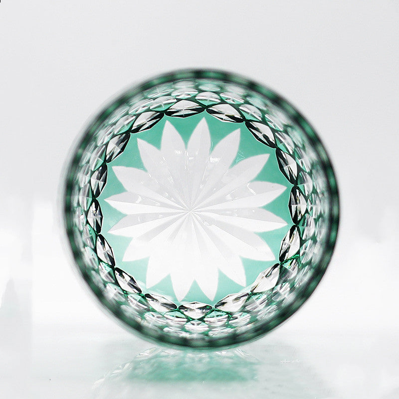 A top view of the Macchiaco Fashion Hand Carved Crystal Glass Cup shows an intricate white and green starburst pattern, framed by a textured, diamond-cut rim.