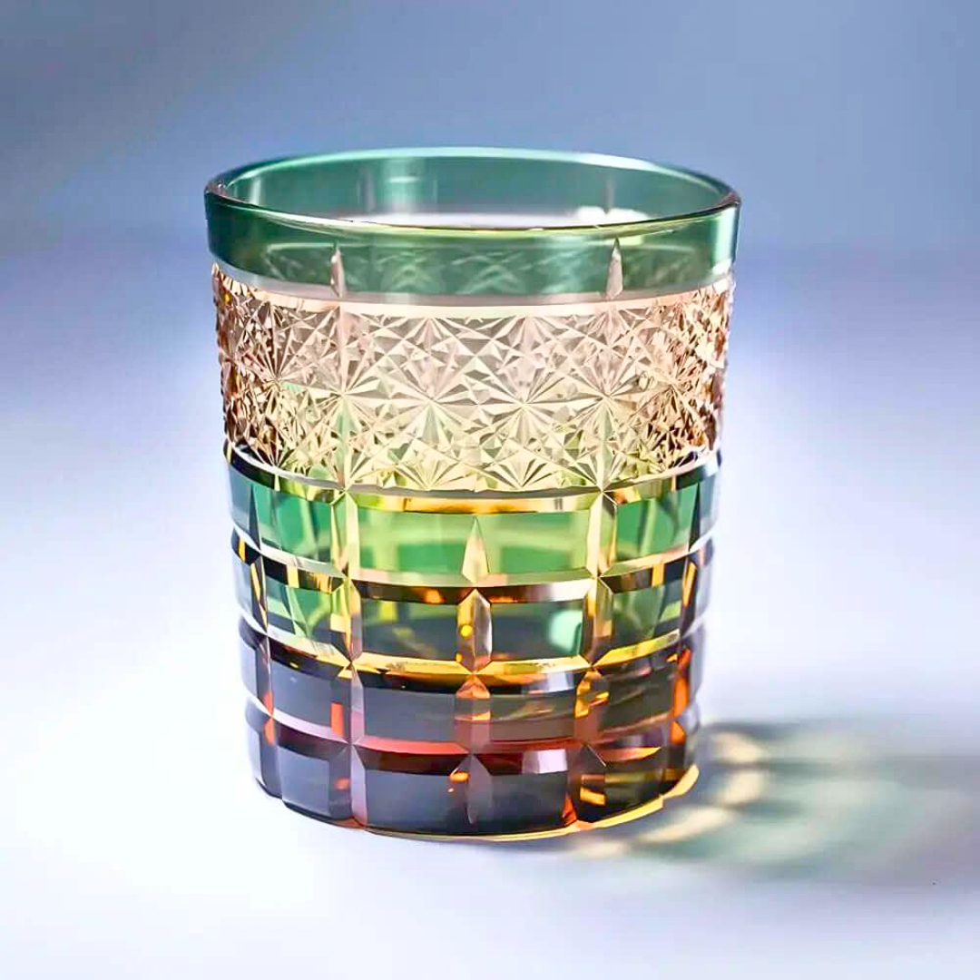 A Crystal Whiskey Glass 8 Oz featuring intricate geometric patterns in green, amber, and clear, showcasing Japanese craftsmanship—perfect for bourbon or scotch—displayed against a neutral background.