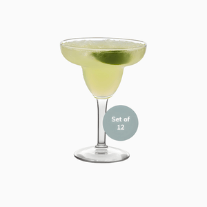 A classic margarita in a stemmed Macchiaco Margarita Glass (Set of 12, 9 oz) with a lime wedge garnish. The glass is labeled “Set of 12”. These durable cocktail glasses are dishwasher safe, shown on a plain white background.